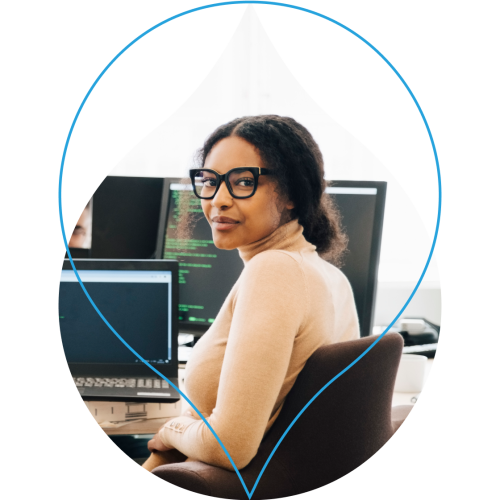 image of a person sitting at a desk with a laptop screen that has code on it masked in an acquia droplet